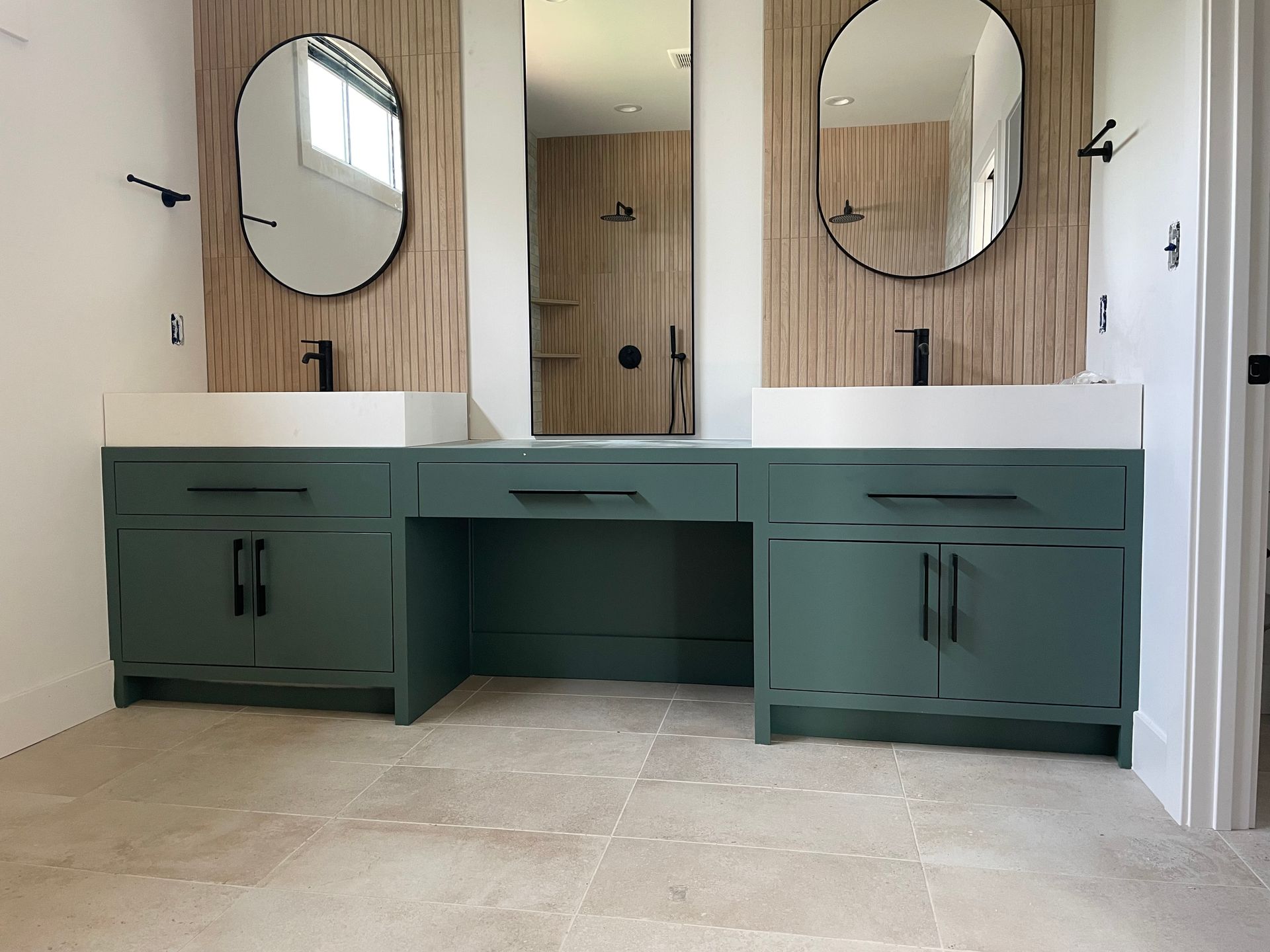 Bathroom vanity with teal cabinets, black fixtures, oval mirrors, and light tile floor.