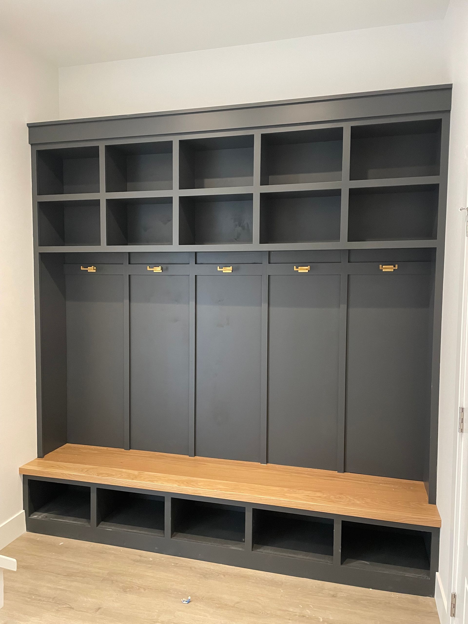 Gray built-in storage unit with open shelves, hooks, and bench. Cork seat, dark gray paint.