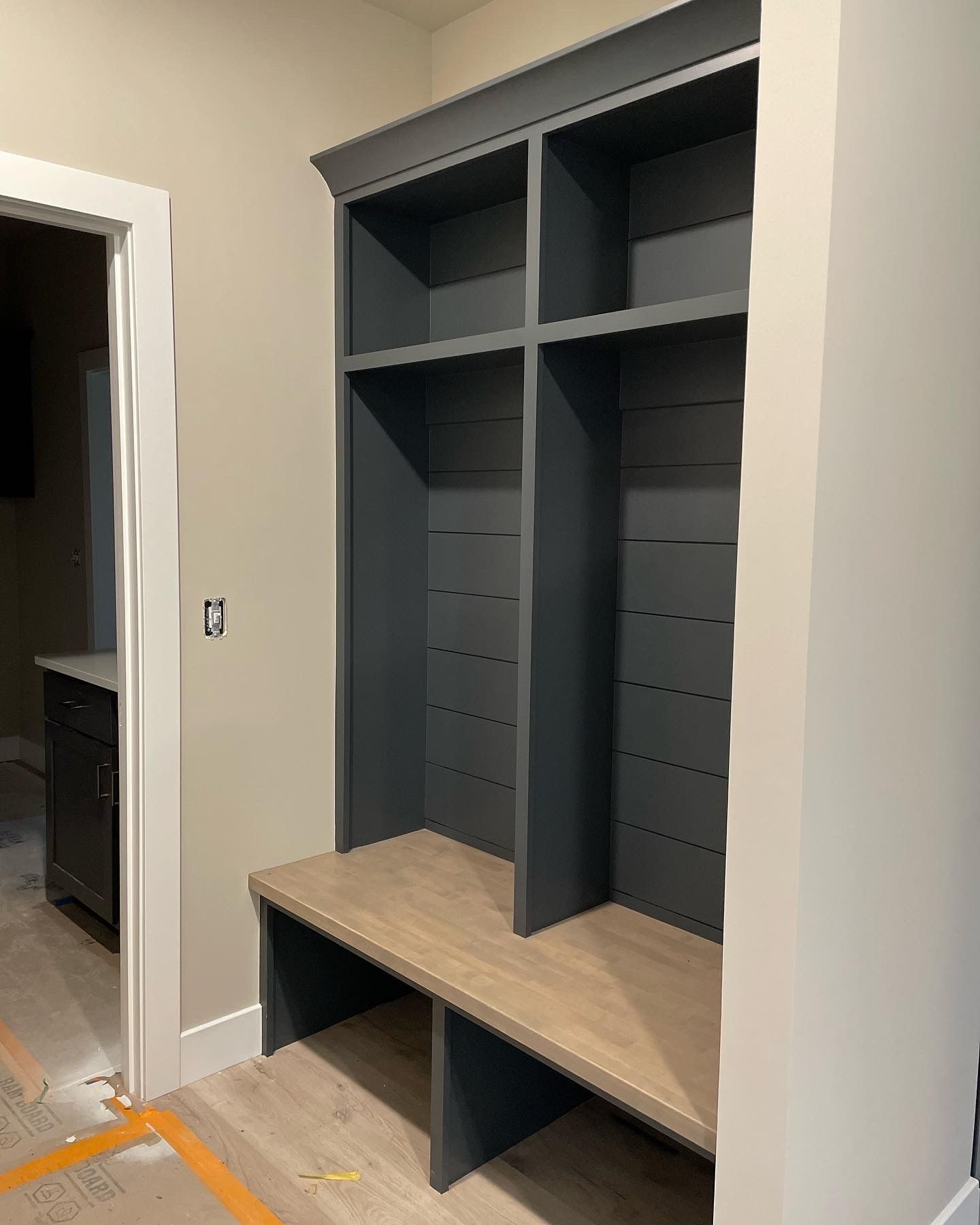 Built-in storage unit with shelves and a bench. Painted dark gray and light wood. Located in a hallway.