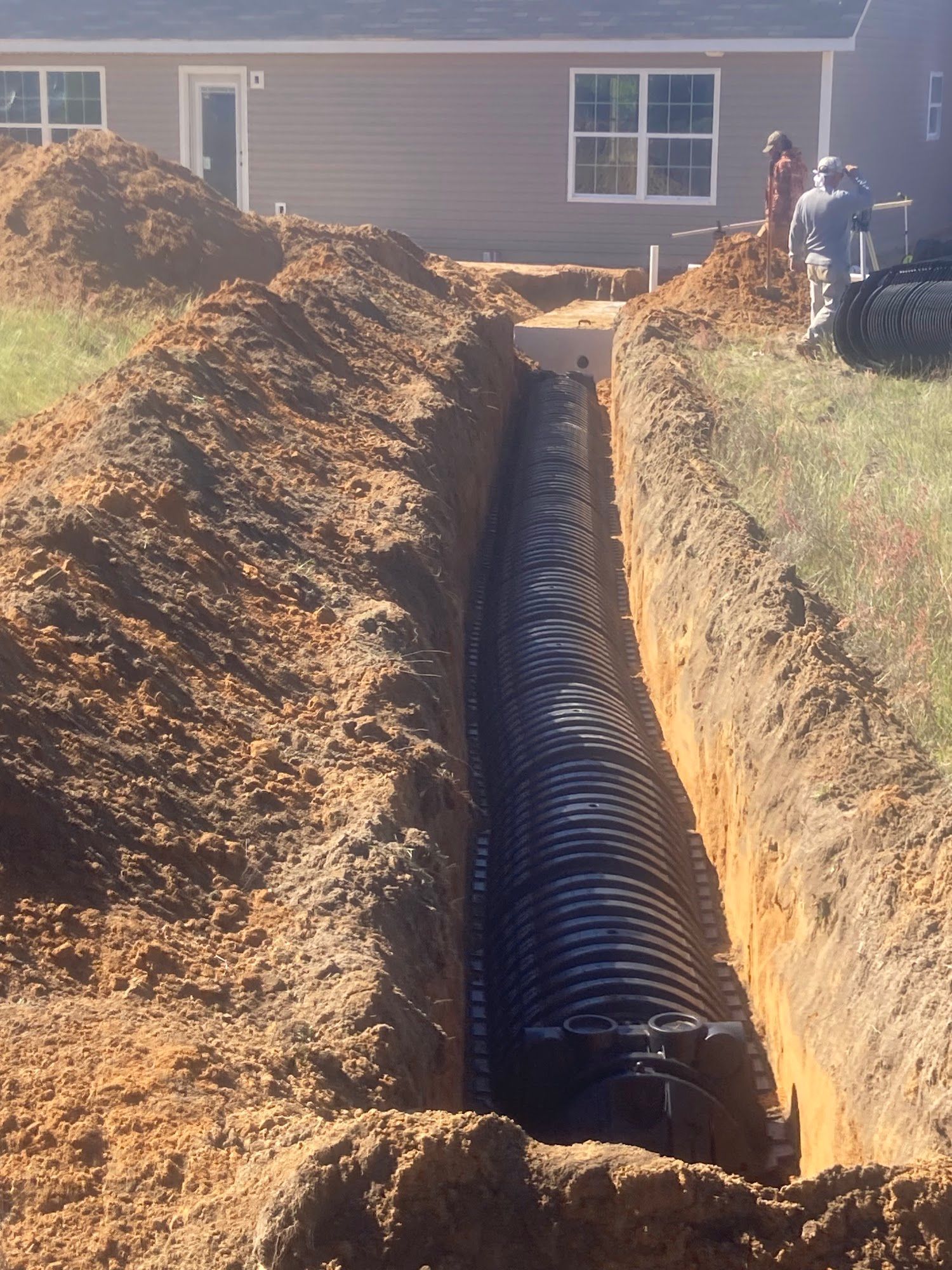 A large pipe is being installed in a trench in front of a house.