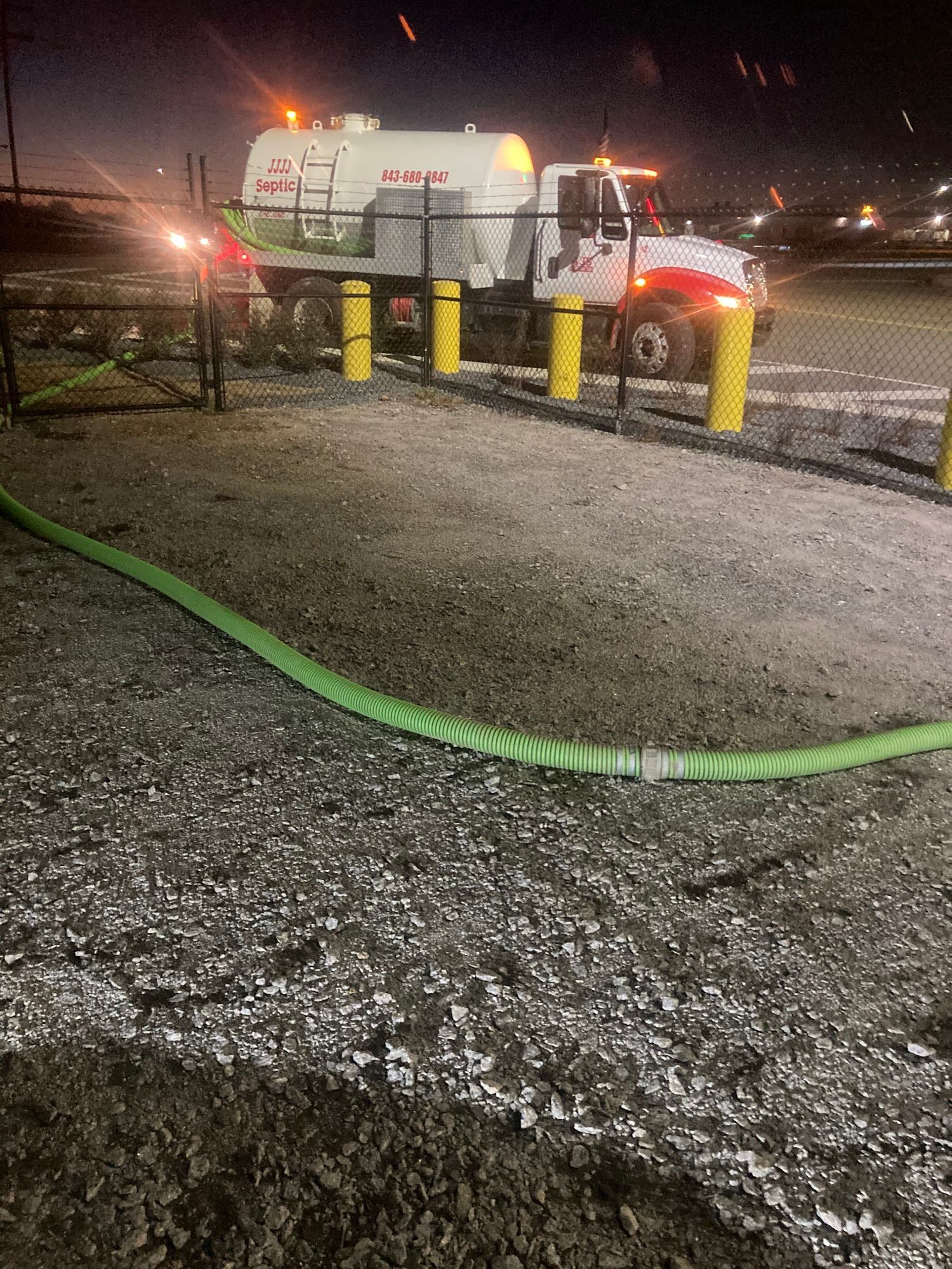 A white truck is parked in a gravel lot with a green hose attached to it.