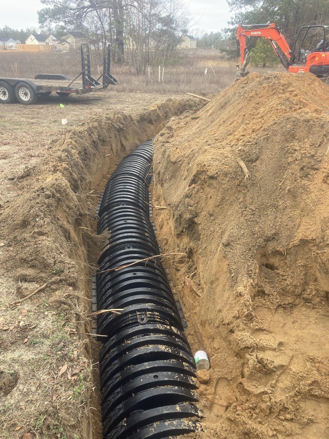 A large black pipe is being installed in the dirt.