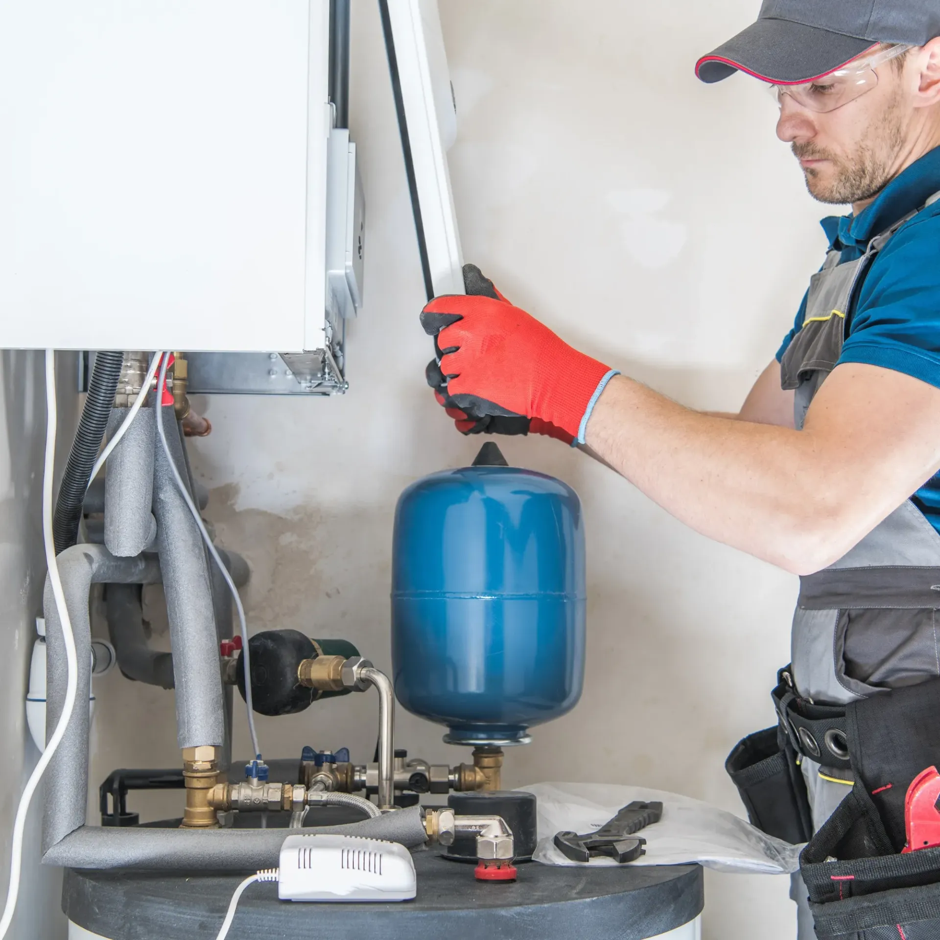 Replacementzone Plumbing - A man wearing red gloves is working on a water heater.