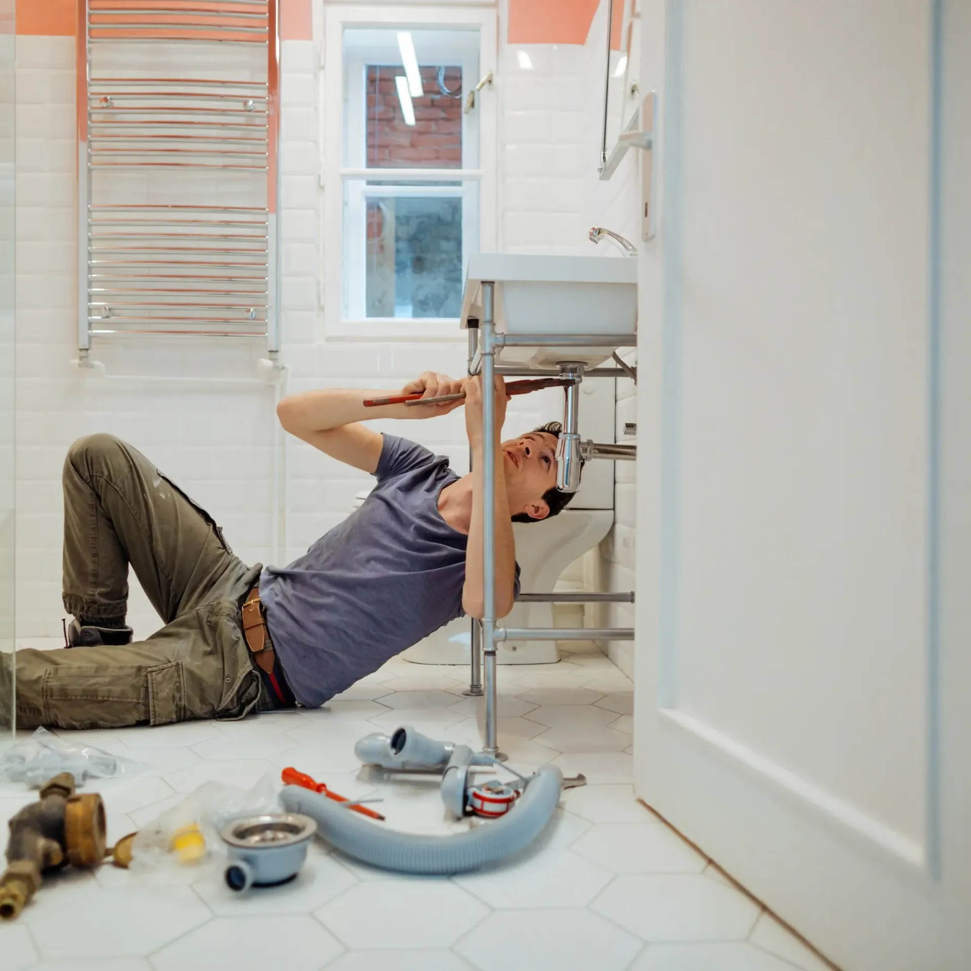 Replacementzone Plumbing -A man is laying on the floor fixing a sink in a bathroom.