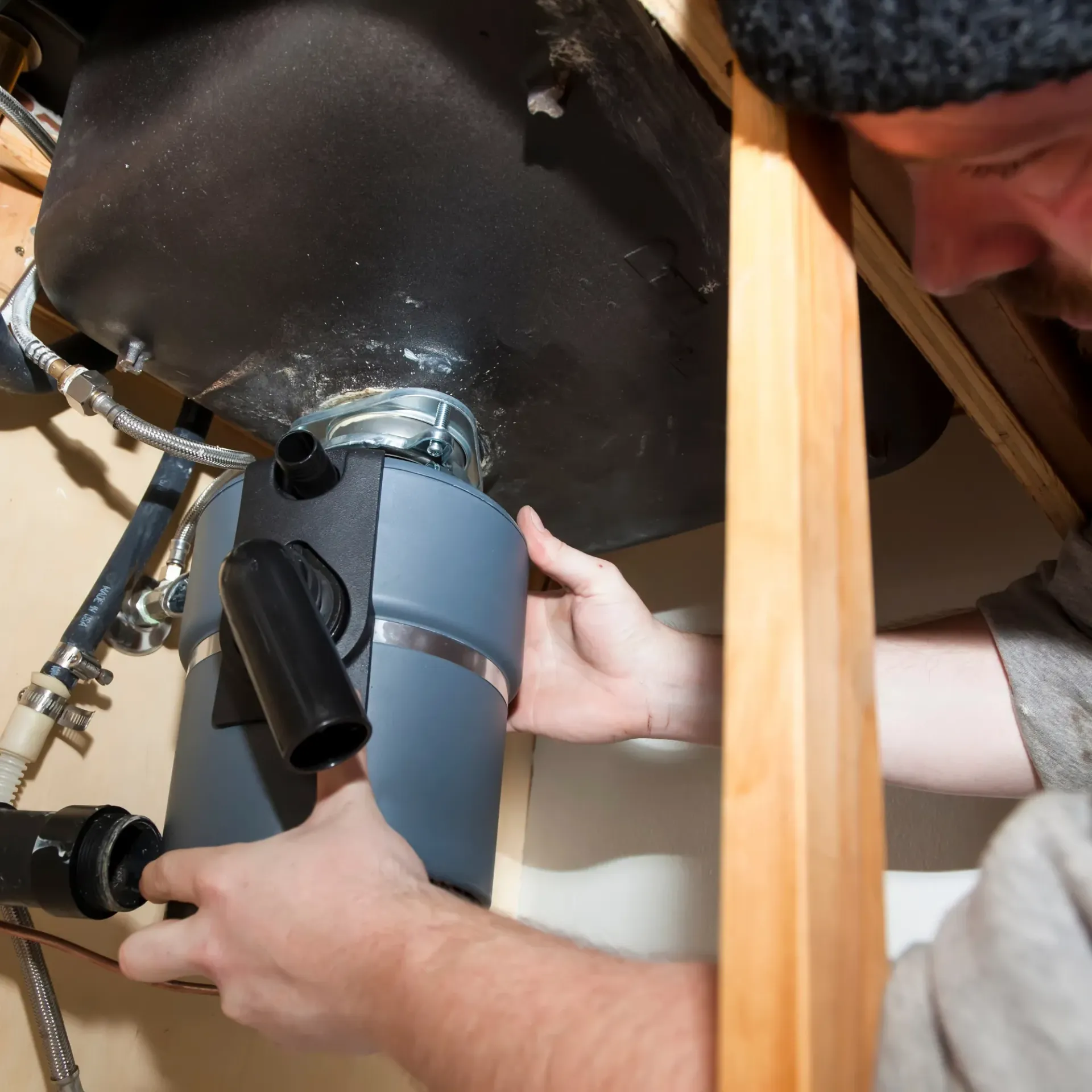 Replacementzone Plumbing - A man is fixing a garbage disposal under a sink