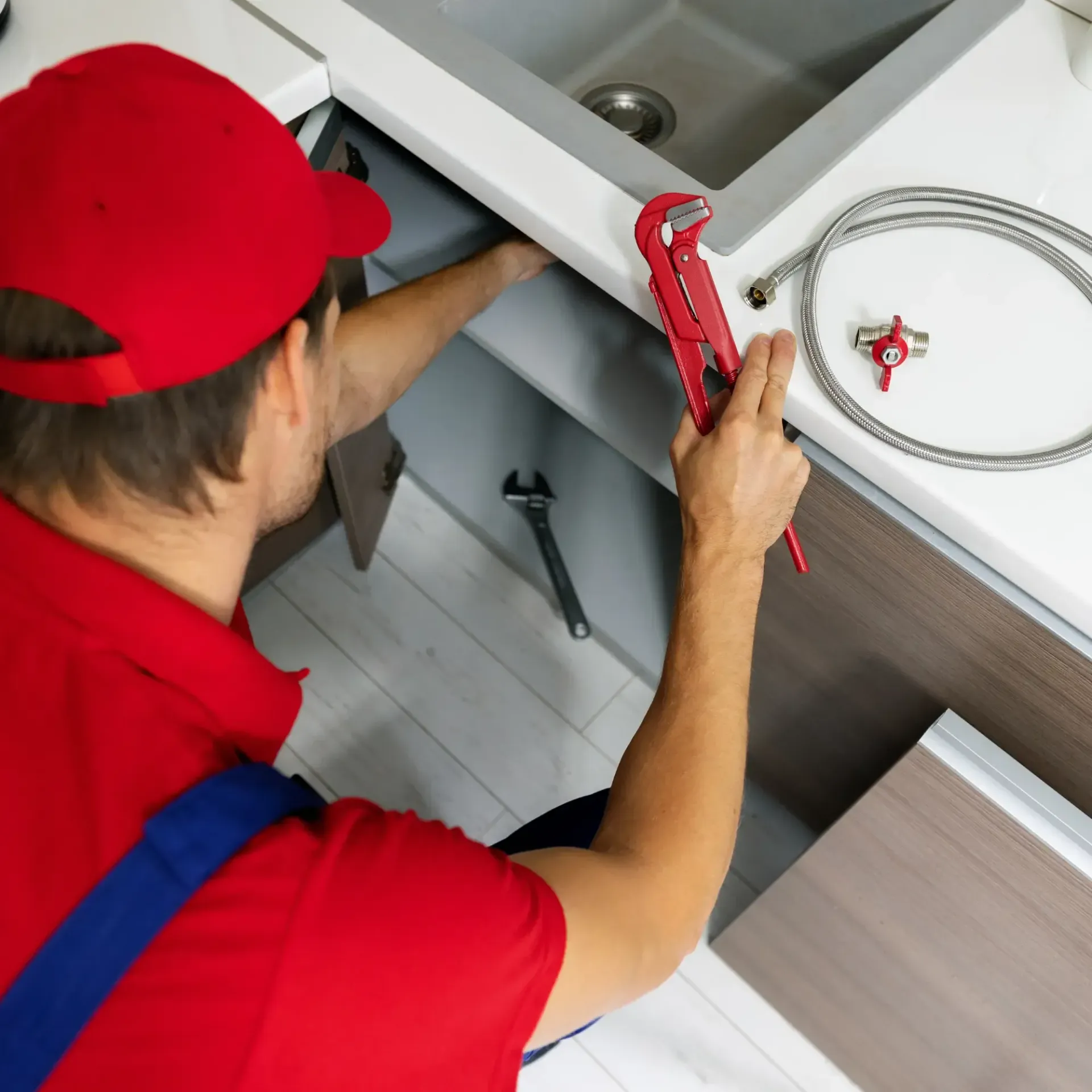ReplacementZone Plumbing  - A man in a red hat is fixing a sink with a wrench