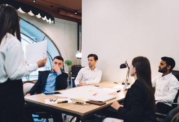 A woman is giving a presentation to a group of people sitting around a table.