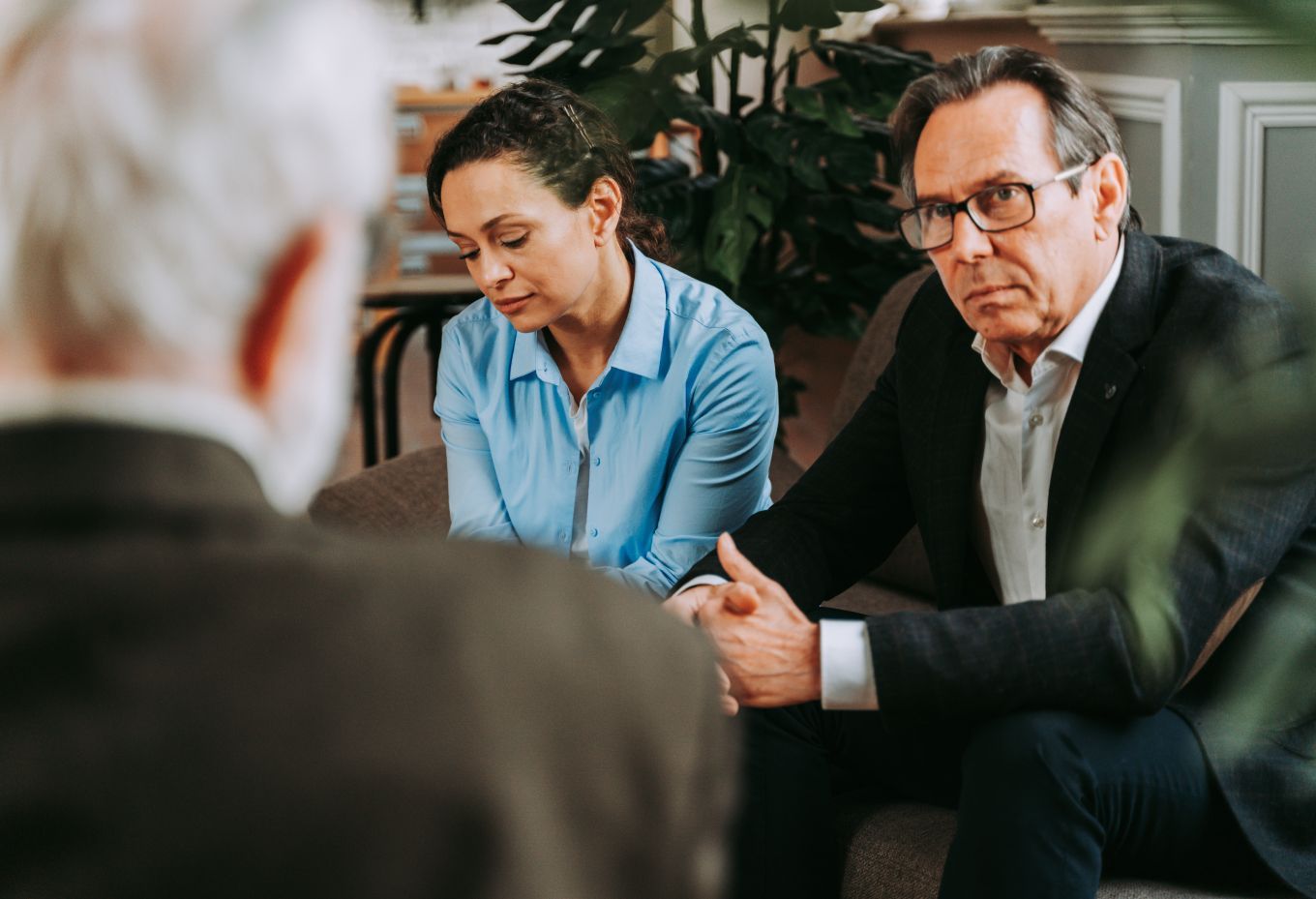 A man and a woman are sitting on a couch talking to a man in a suit.