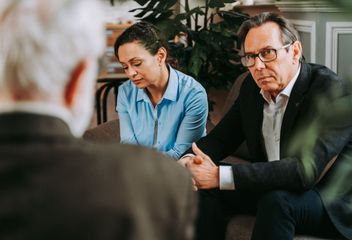 A man and a woman are sitting on a couch talking to a man in a suit.