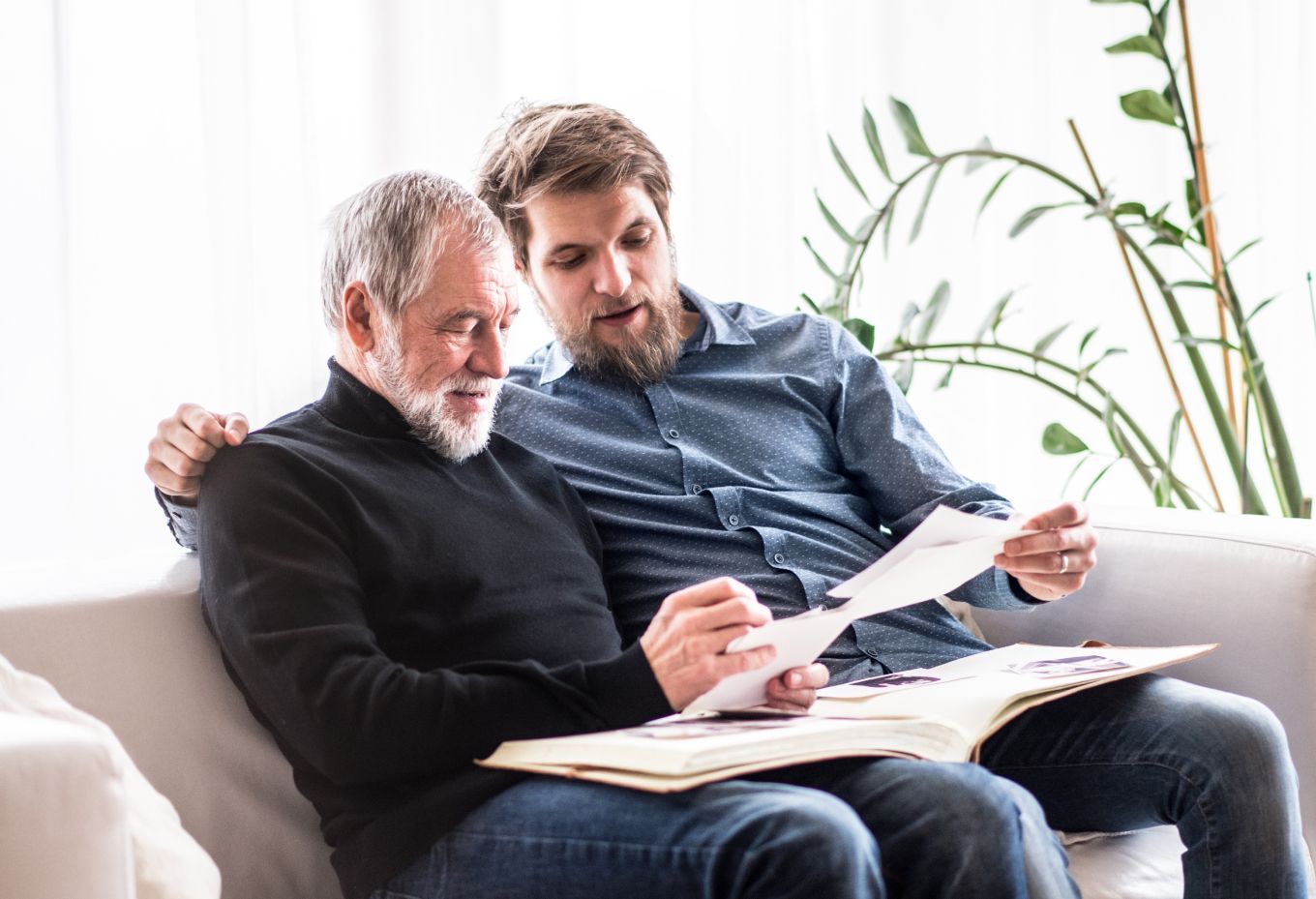 Two men are sitting on a couch looking at a book.