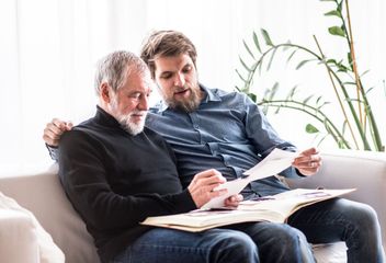 Two men are sitting on a couch looking at a book.