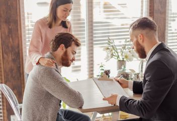 A man and a woman are sitting at a table talking to a man in a suit.