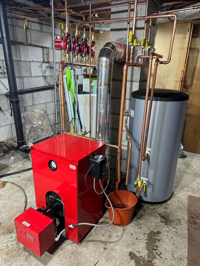 Red boiler and gray water heater with copper pipes in a utility room