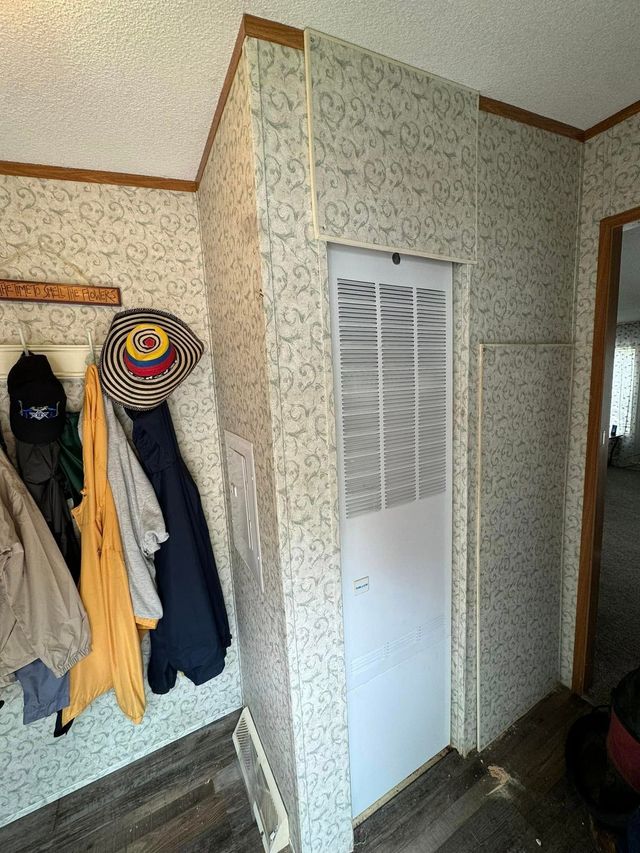 Entryway with coats on hooks, a white louvered door, patterned wallpaper, and a colorful hat rack