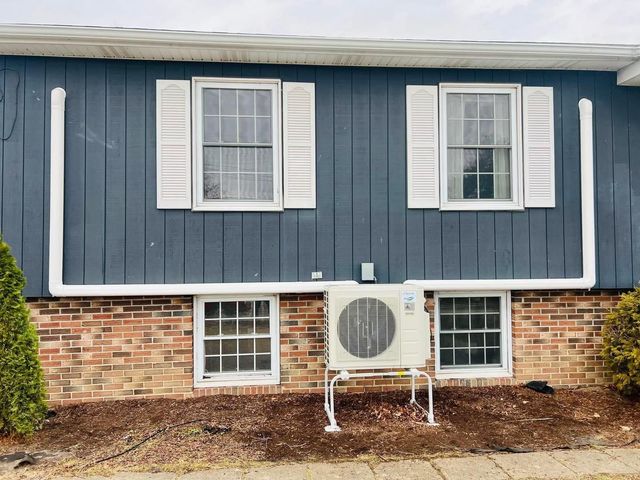 House exterior with blue siding, white shutters, brick base, and a visible air conditioner unit.