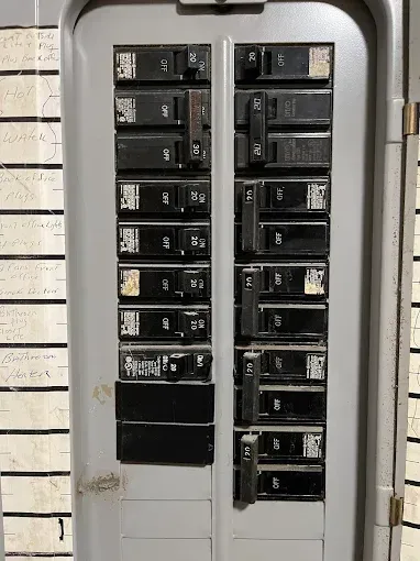 Electrical breaker panel with multiple black switches in a gray metal box