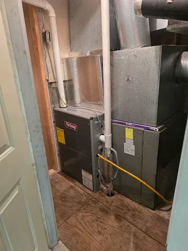 Two HVAC furnaces in a narrow utility closet with ductwork and pipes along the wall