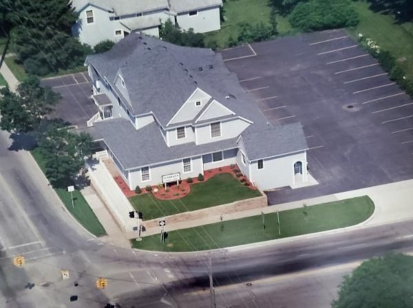 Aerial view of a two-story white building with a parking lot, trees, and a street corner.