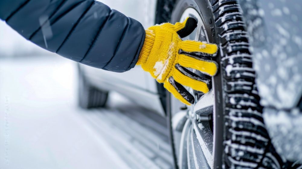 Een persoon met gele handschoenen verwisselt een band op een besneeuwde weg.