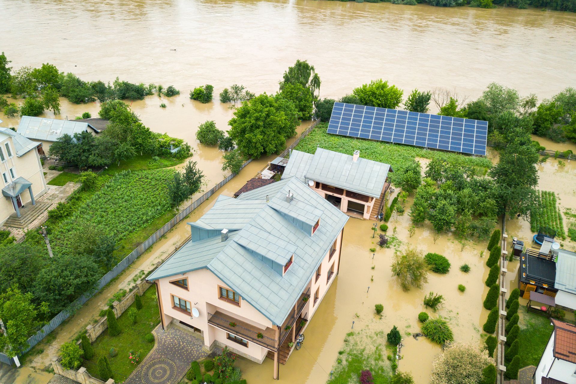 Vue aérienne d'une maison entourée d'eaux de crue boueuses avec des panneaux solaires.