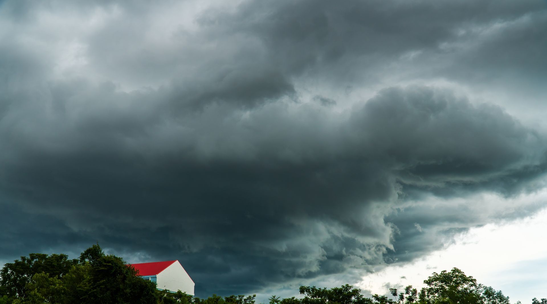 De sombres nuages d'orage s'accumulent au-dessus d'une maison au toit rouge et d'arbres verts