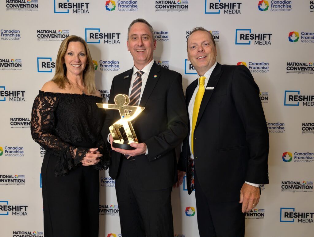 Three people holding a trophy at a RESHIFT awards event backdrop