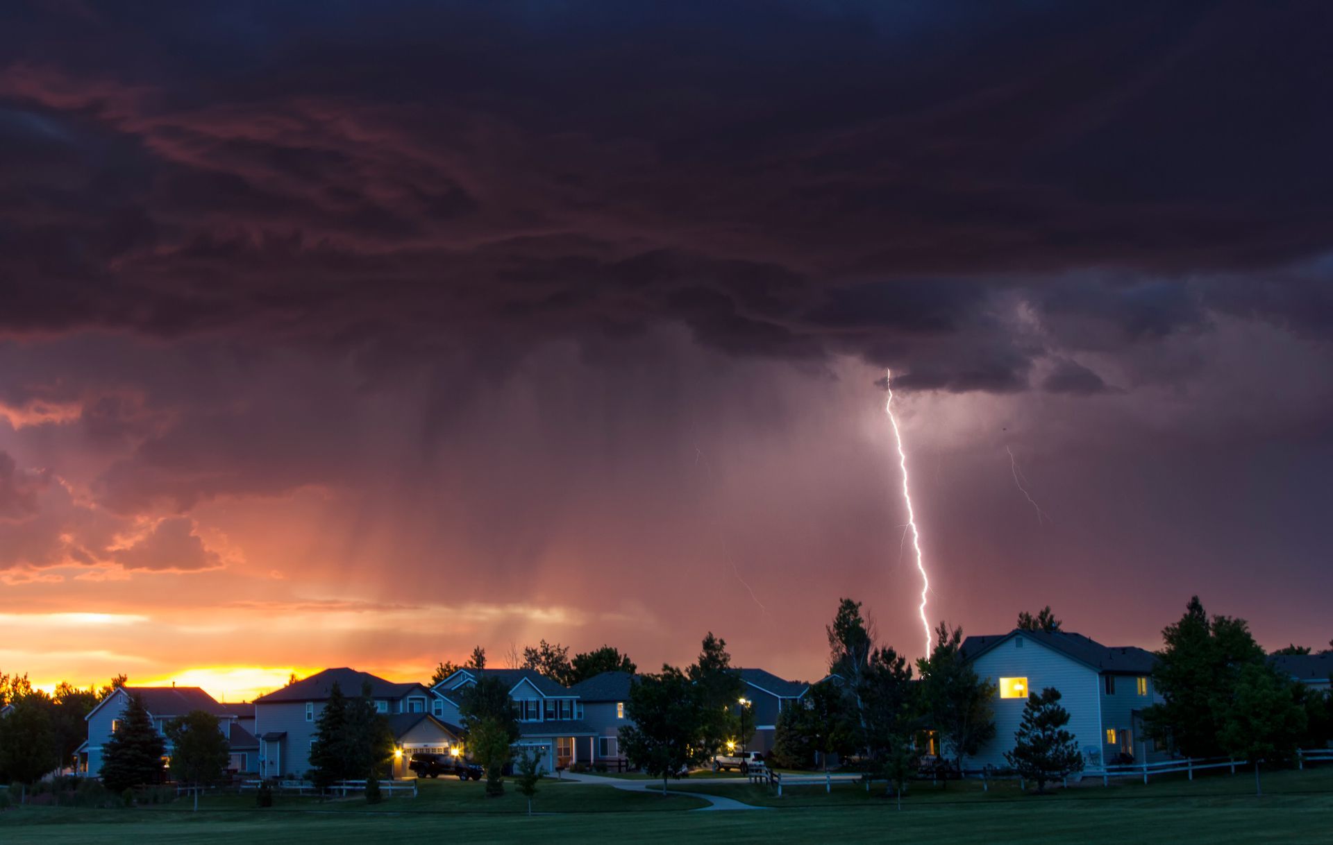Lightning strikes near suburban homes during a summer storm at sunset.