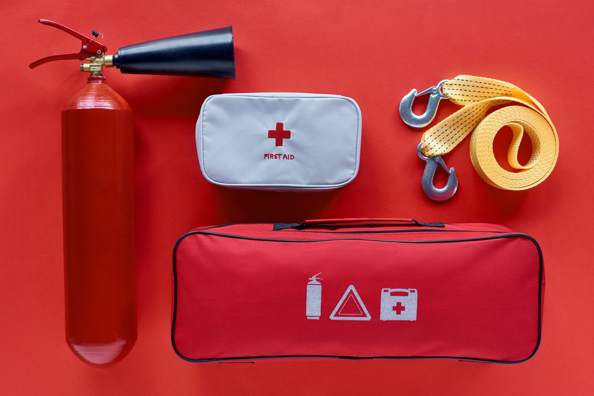 Trousse d’urgence avec extincteur, premiers soins et sangle de remorquage sur fond rouge.