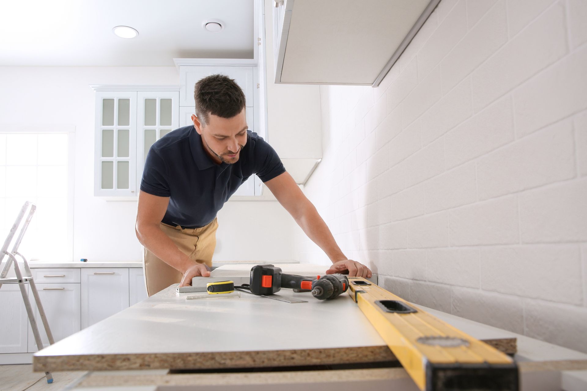 A person installing a countertop in a kitchen with a drill and a spirit level on the surface.