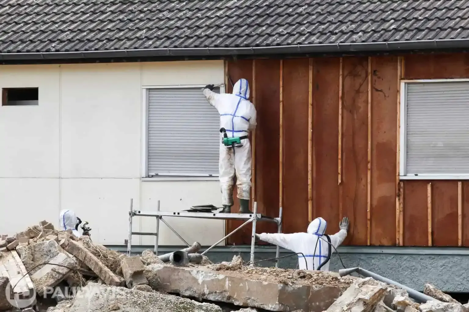 Technicians in full PPE removing siding from older home during professional asbestos remediation.