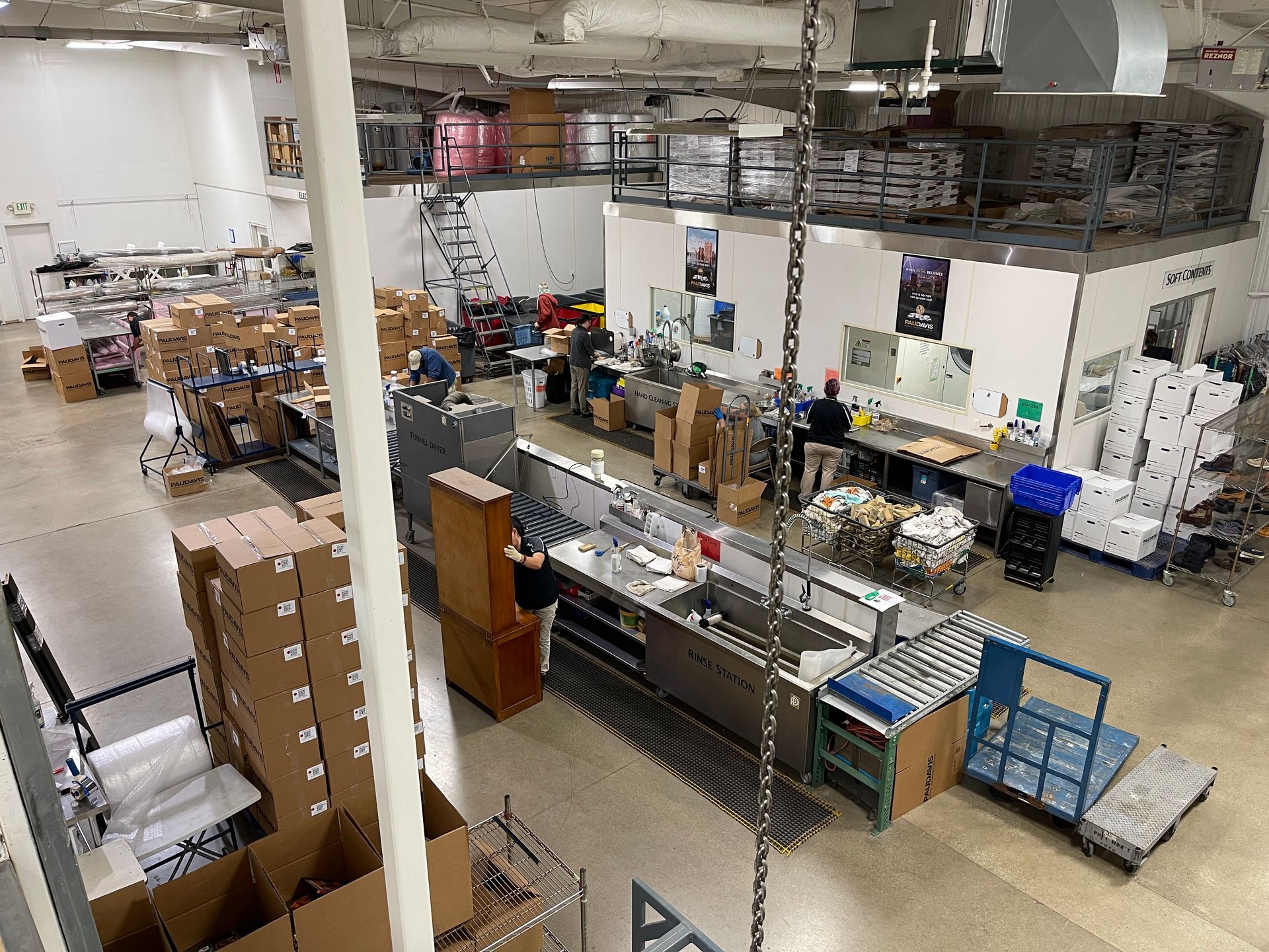 High-angle view of a busy warehouse with boxes, equipment, workstations, and staff working in an open industrial space.