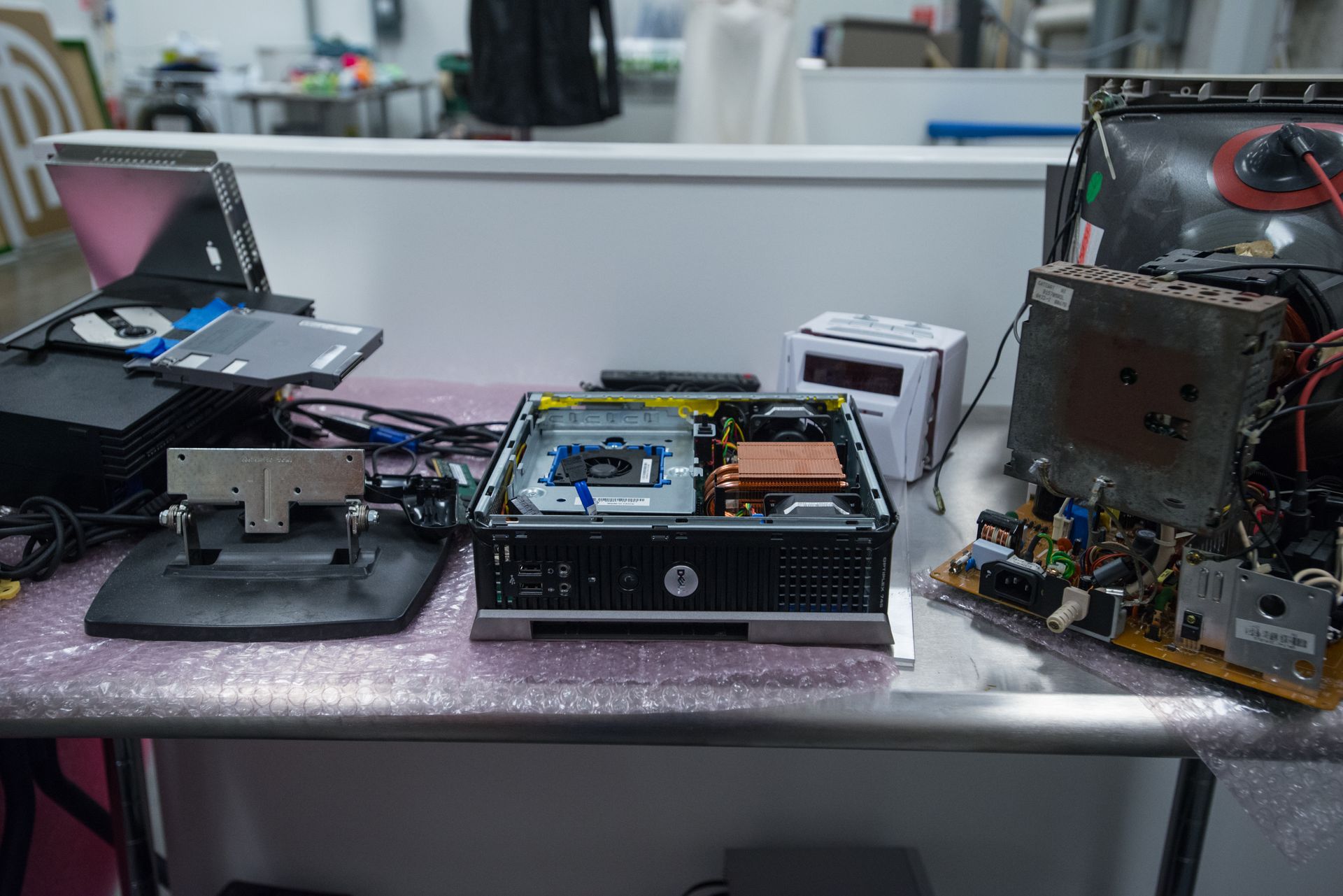 Disassembled computer components and an open monitor chassis spread out on a table in a workspace.