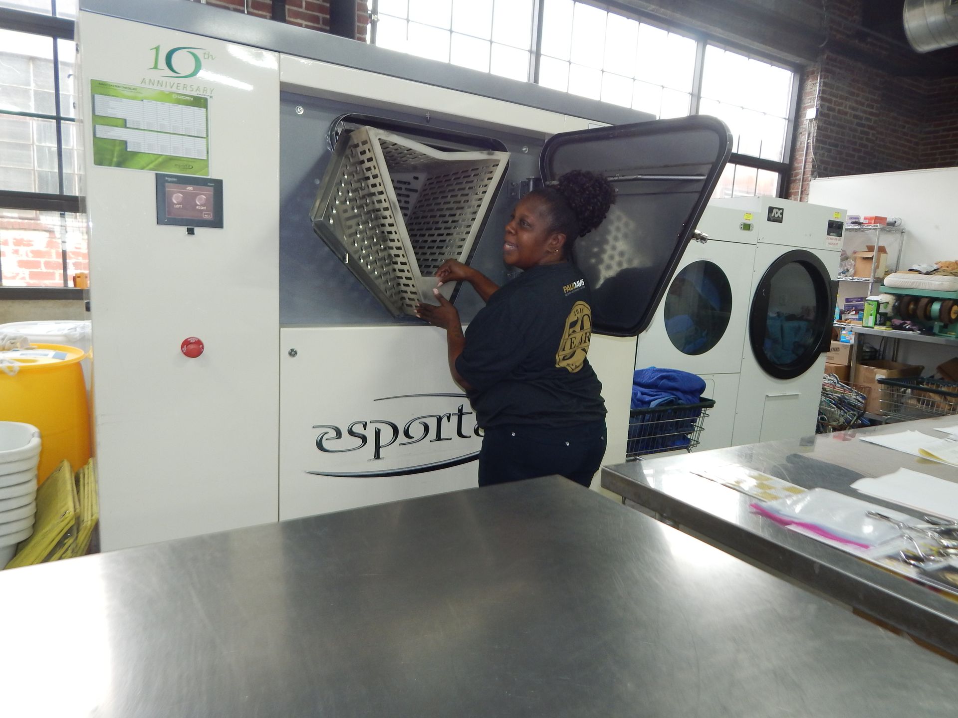 A worker loads a metal basket into an Esporta industrial washing machine in a commercial laundry facility.