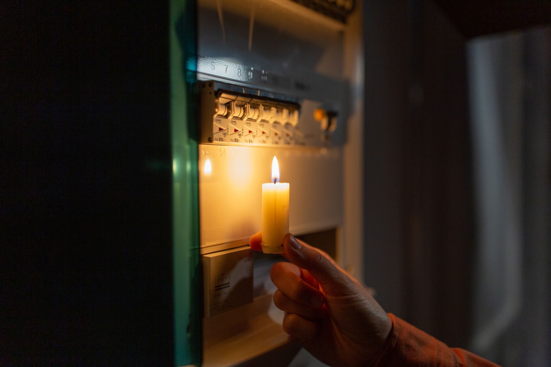 Personne tenant une chandelle près d’un panneau électrique pendant une panne en hiver.