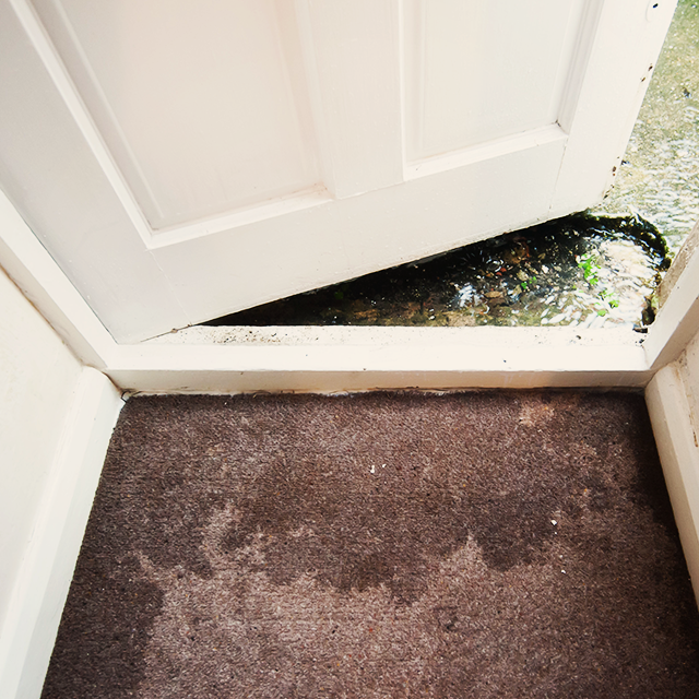 Water flowing under a white door, soaking a dark brown door mat.