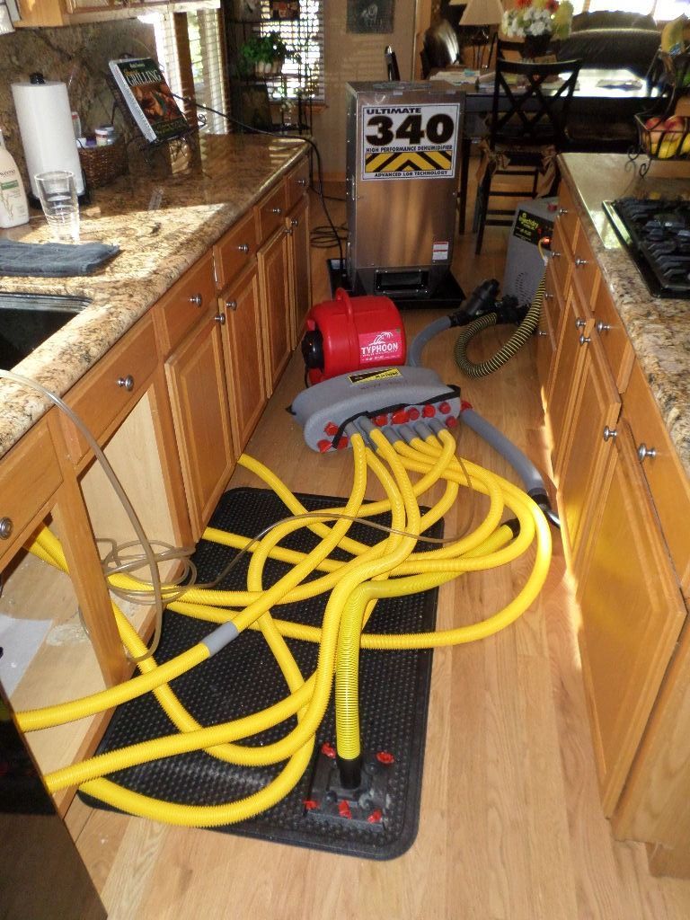 Industrial floor drying equipment with yellow hoses and a dehumidifier setup in a residential kitchen.