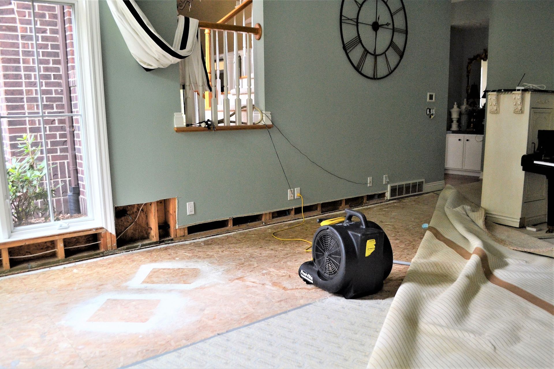 Flood-damaged living room with drywall removed and floor drying equipment in use during restoration.
