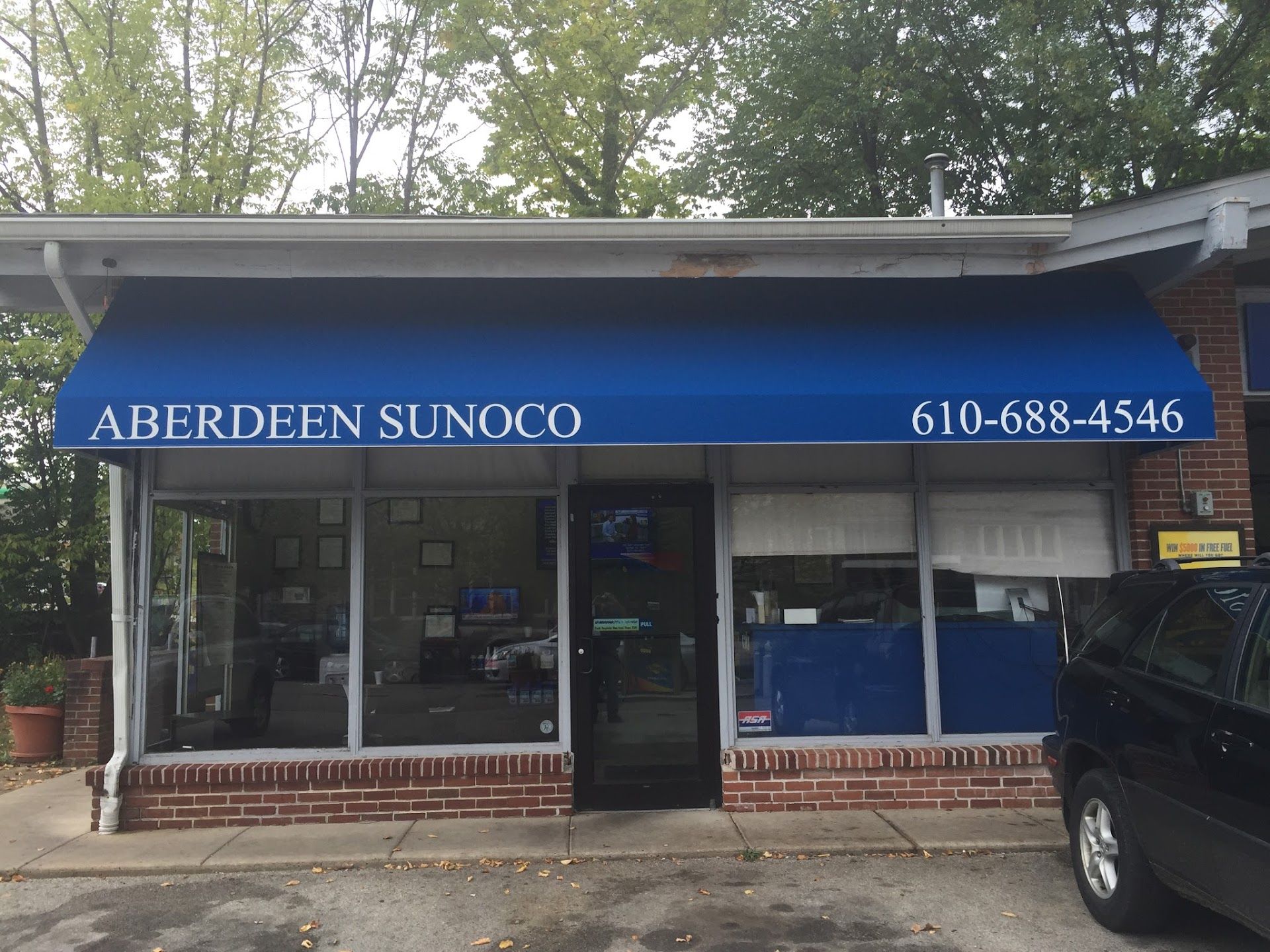 Gas price sign at Sunoco: Regular gas $2.23, Ultra 93 $2.63. Brick columns, traffic light, and cars in background. | Aberdeen Automotive