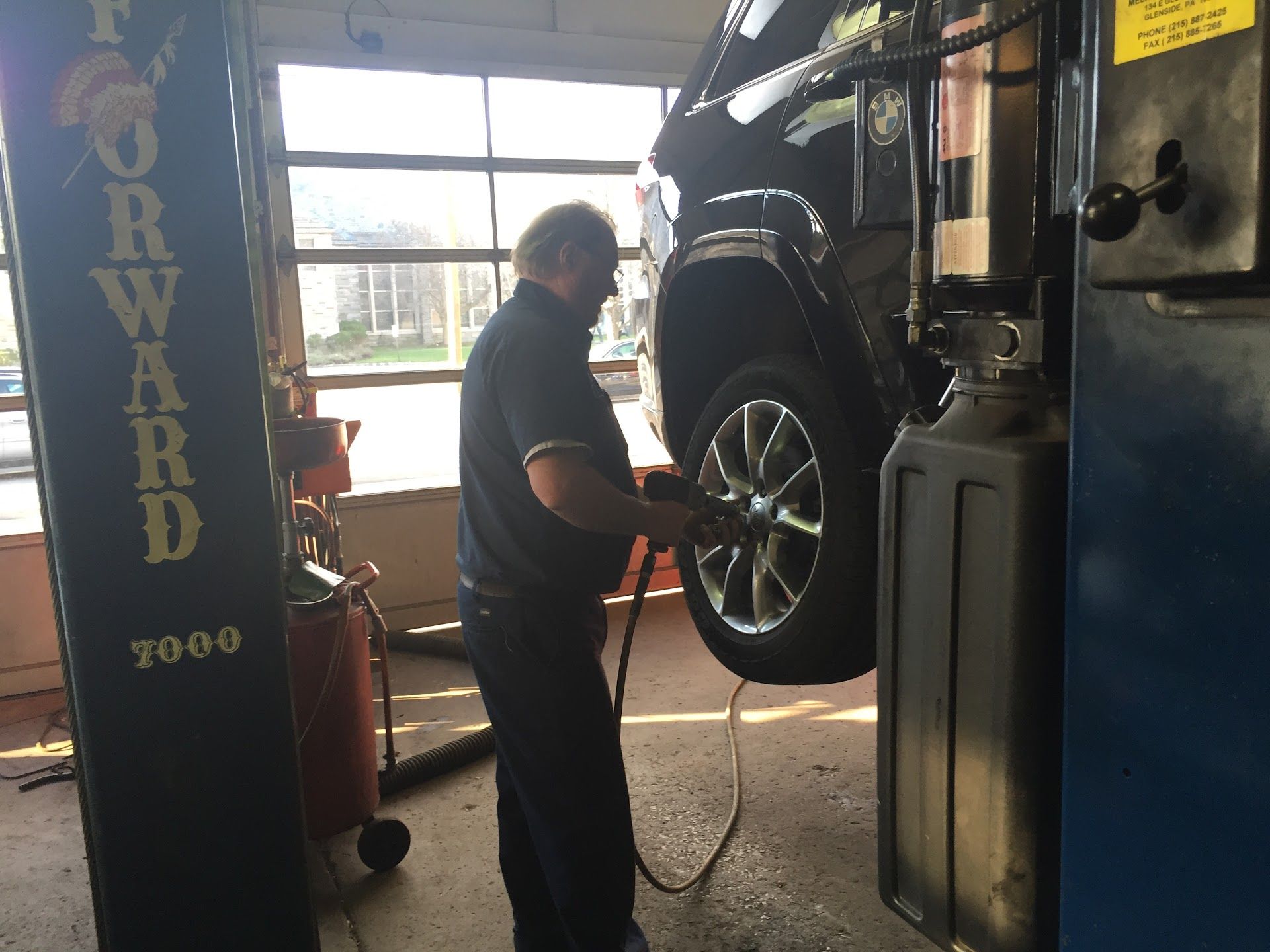 Mechanic using an air hose on a car tire, in a garage with a car lift. | Aberdeen Automotive