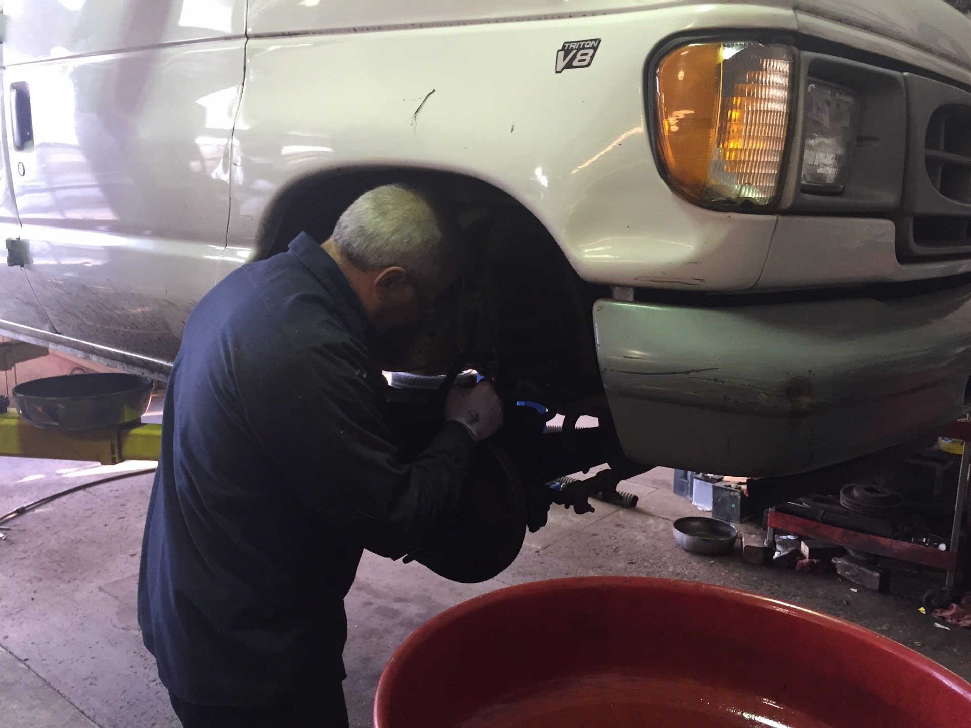 Mechanic working on the front wheel of a white van in a garage, using a tool. A red tub is on the floor. | Aberdeen Automotive