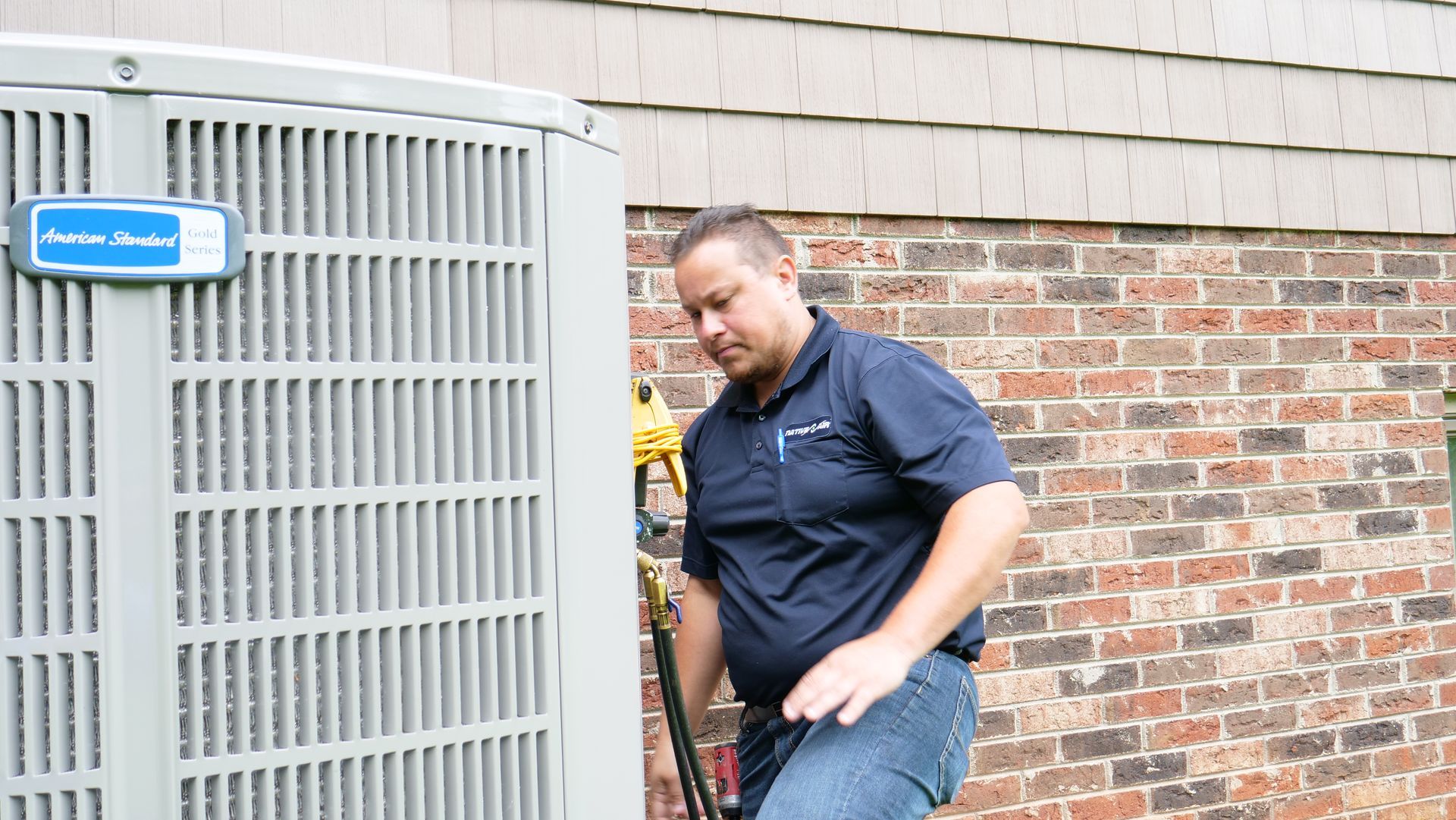 A man is working on an air conditioner outside of a brick building.