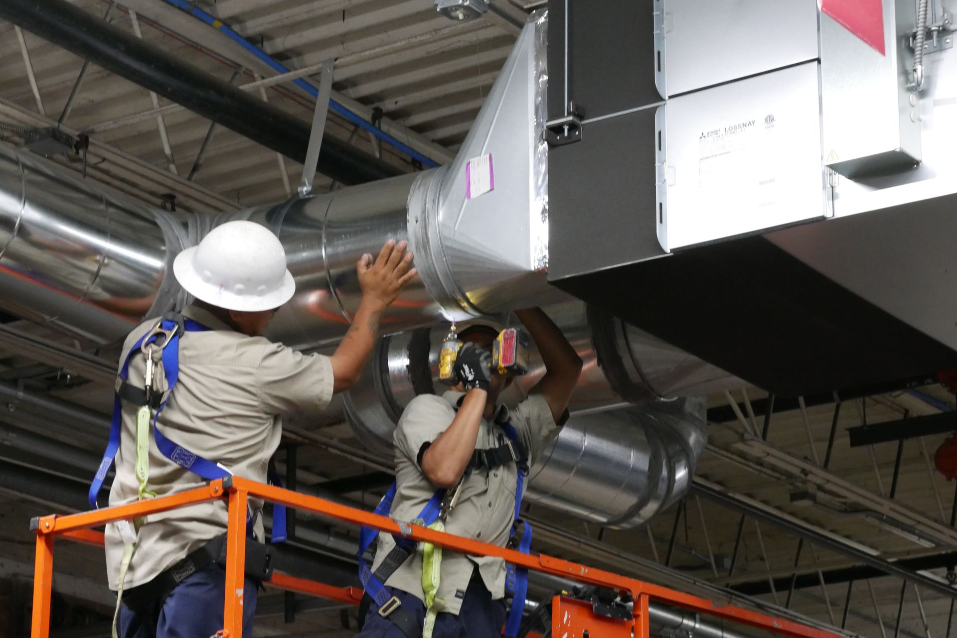 Two men are working on a ventilation system in a building.