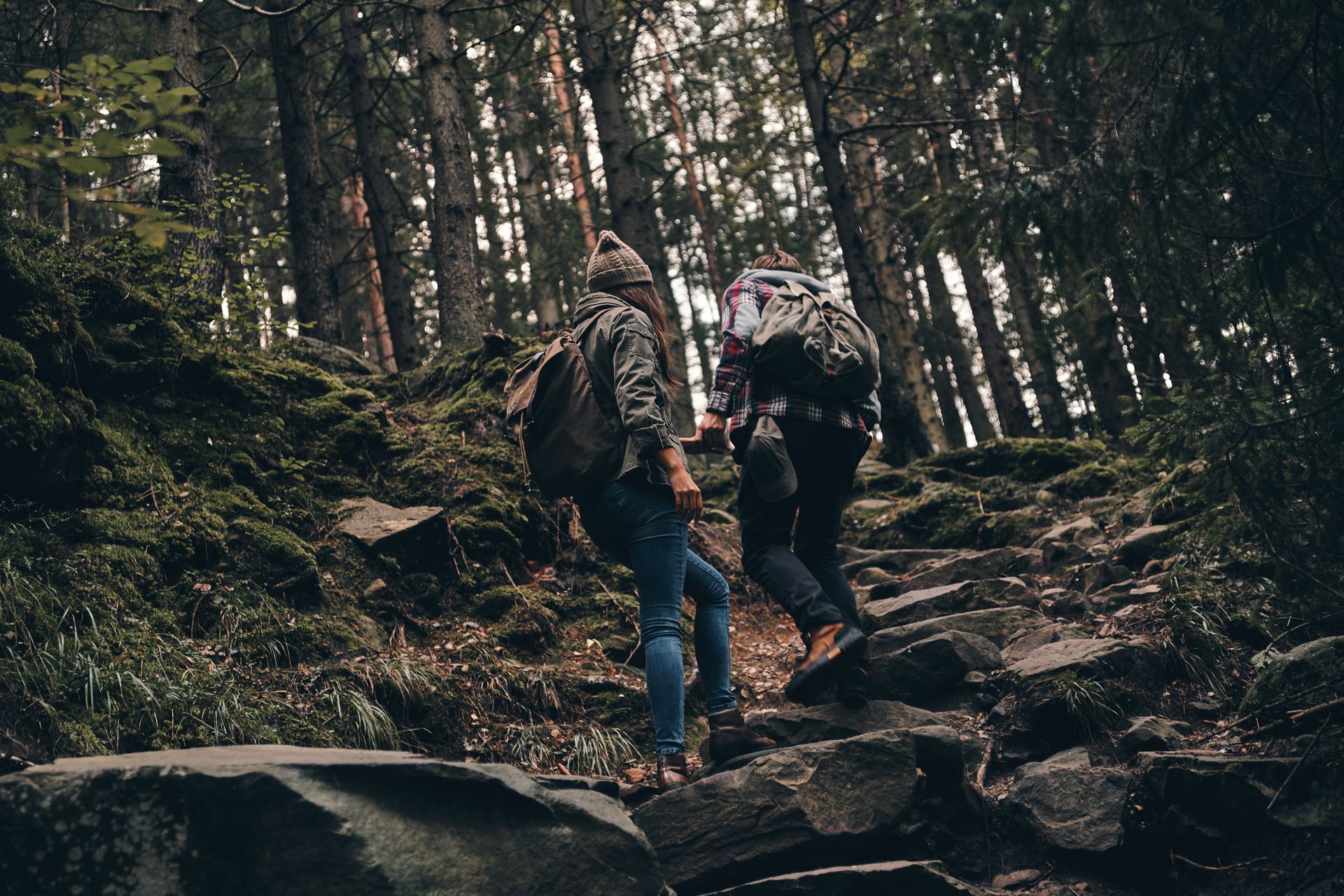 Two hikers ascending a rocky, mossy forest trail. Trees surround them.