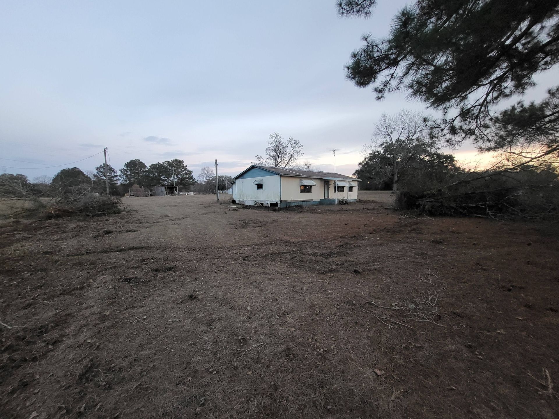 Dilapidated, single-story house in a clearing; overcast sky.