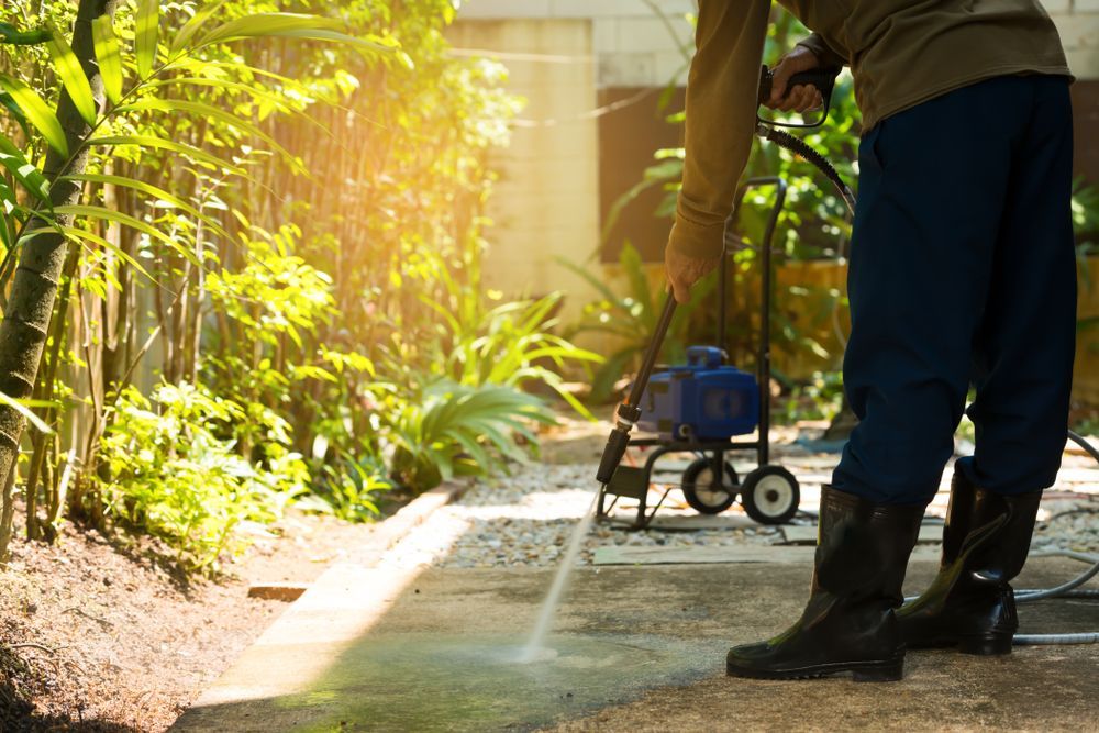 A Man Is Using A High Pressure Washer To Clean A Sidewalk — Lindfield’s Big Red Carpet Cleaning & Pest Control in Harrington, NSW
