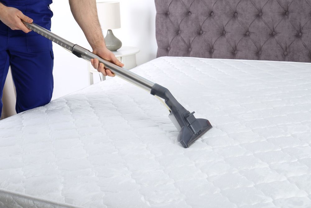 A Man Is Cleaning A Mattress With A Vacuum Cleaner — Lindfield’s Big Red Carpet Cleaning & Pest Control in Tallwoods Village, NSW