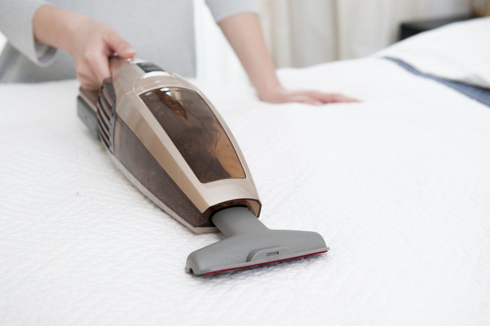 A Person Is Using A Vacuum Cleaner To Clean A Bed — Lindfield’s Big Red Carpet Cleaning & Pest Control in Taree, NSW