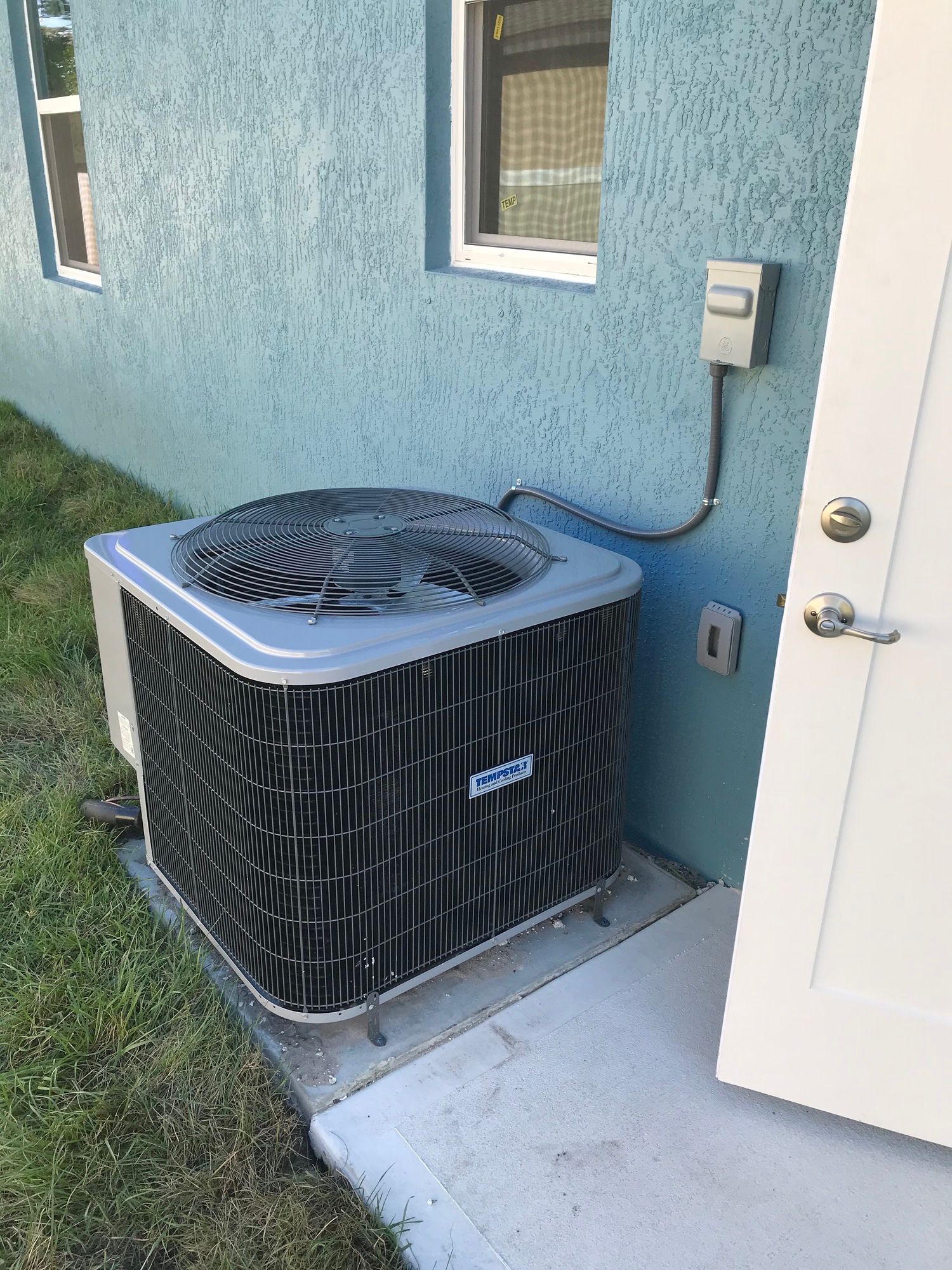 An air conditioner is sitting outside of a house next to a door.