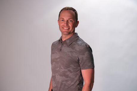 Smiling man in a gray patterned polo shirt standing against a white background