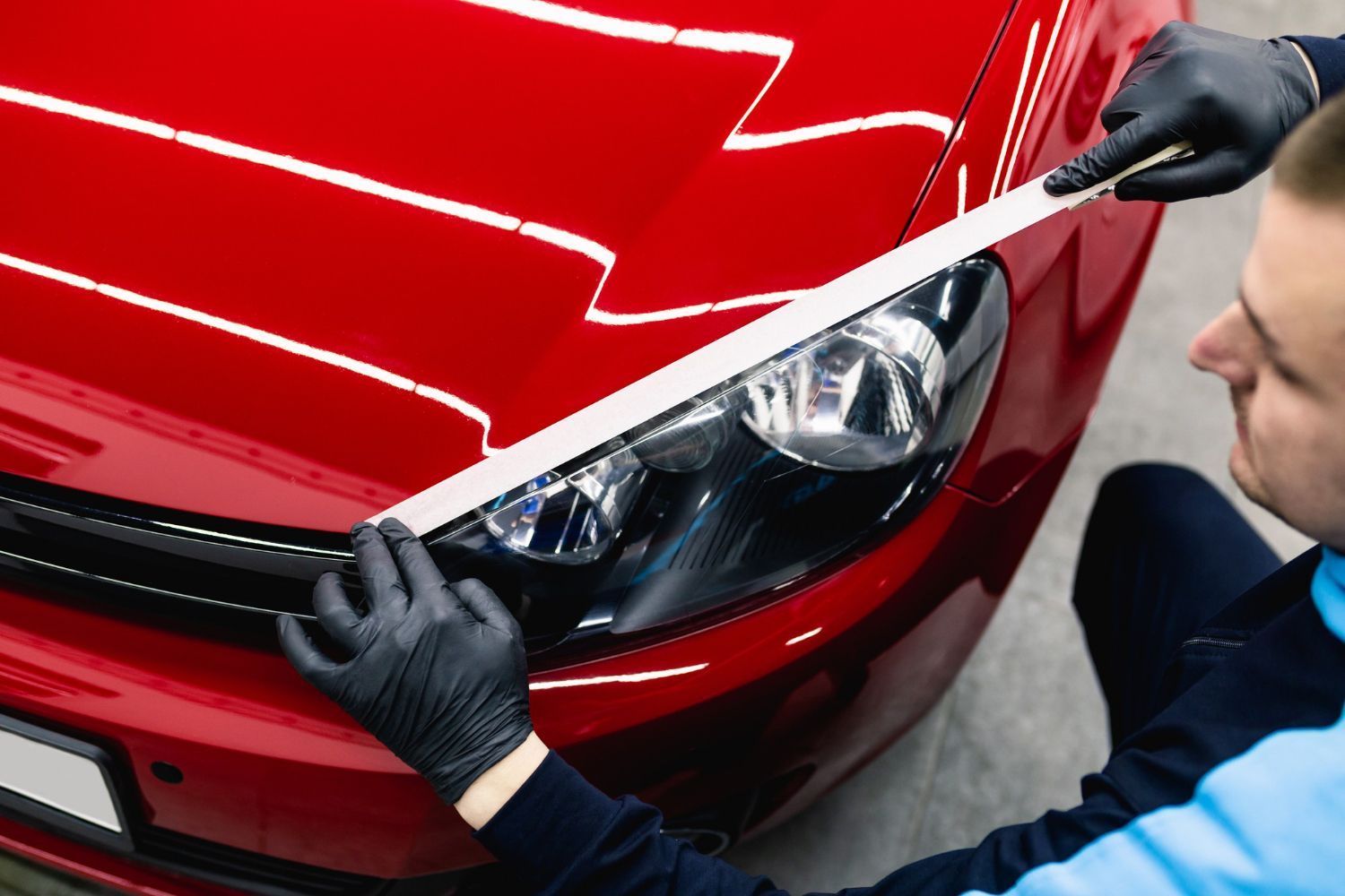 A man is cleaning the headlights of a red car.
